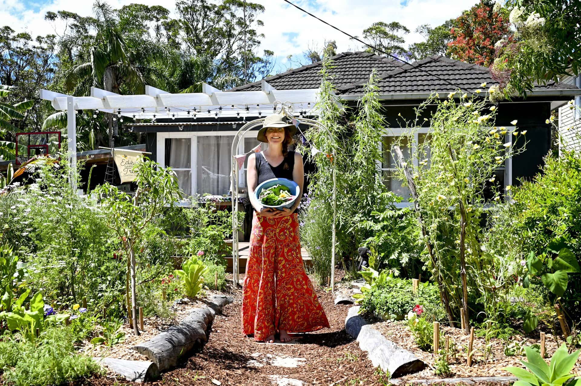 Lorrae holding a bowl of freshly picked salad in front of her house